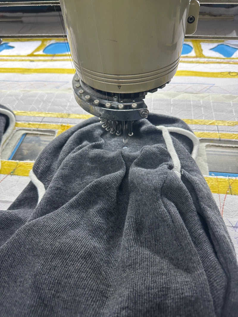 Close-up of embroidery machine head at BENTA factory, processing grey knitwear fabric for OEM custom embroidery apparel.