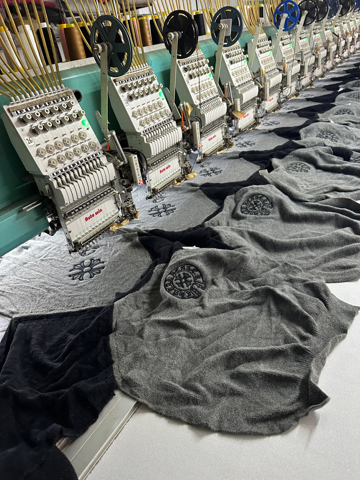 Row of multi-head automatic embroidery machines at BENTA factory, embroidering patterns on knitwear blanks for OEM custom clothing production.