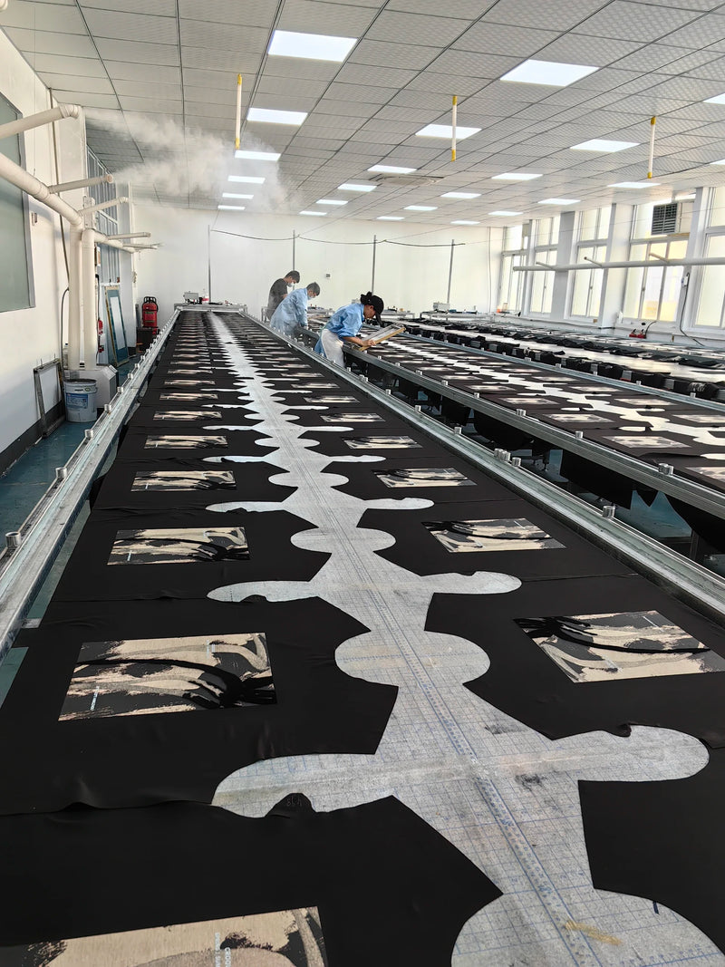 Wide shot inside BENTA factory workshop, workers inspecting black crochet fabric panels laid on long conveyor production tables for OEM custom apparel manufacturing.