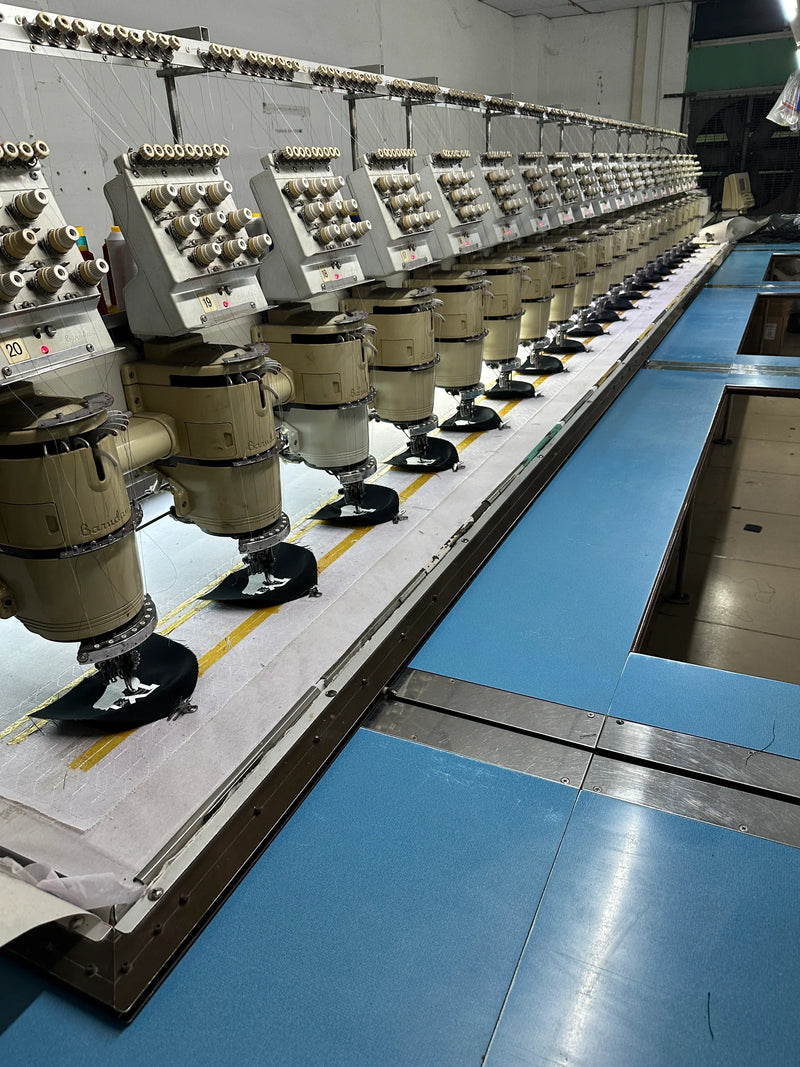 Long full row of multi-head automatic embroidery machines inside BENTA knitwear OEM factory workshop, showing large-scale automated crochet fabric production equipment.