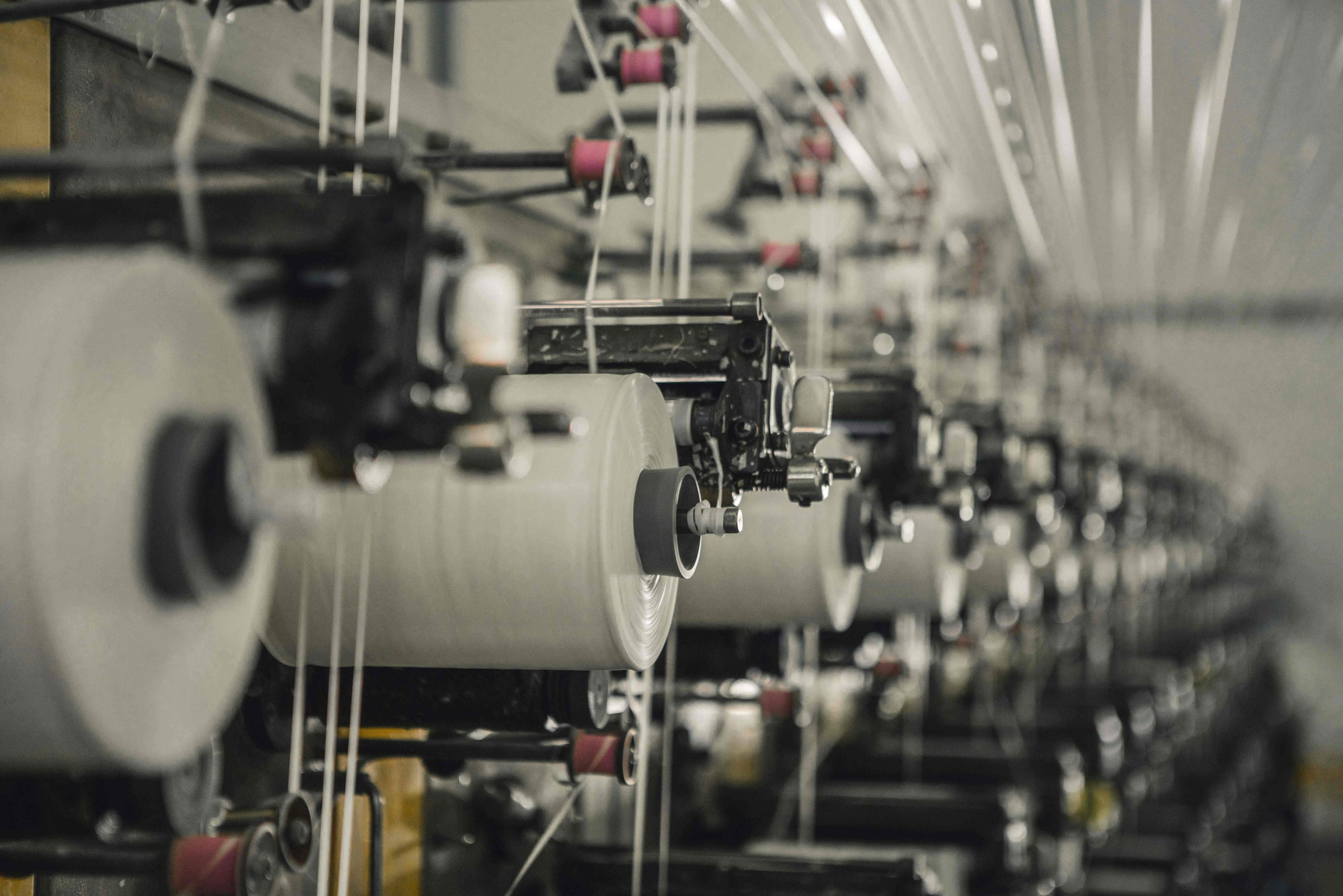 Close-up view of industrial knitting machines with rows of yarn spools inside BENTA knitwear OEM production workshop.