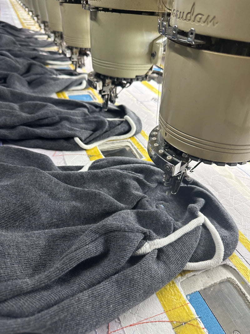 Row of multi-head automatic embroidery machines at BENTA factory, embroidering patterns on grey knitwear garments for OEM custom knit clothing production.