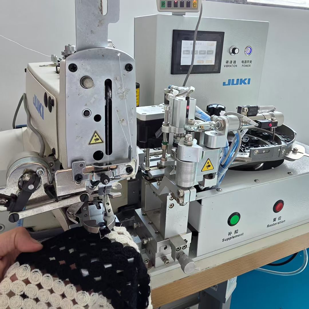 Close-up of worker operating JUKI automatic button attaching machine in BENTA factory, processing black and white hollow crochet knit fabric for OEM custom apparel.