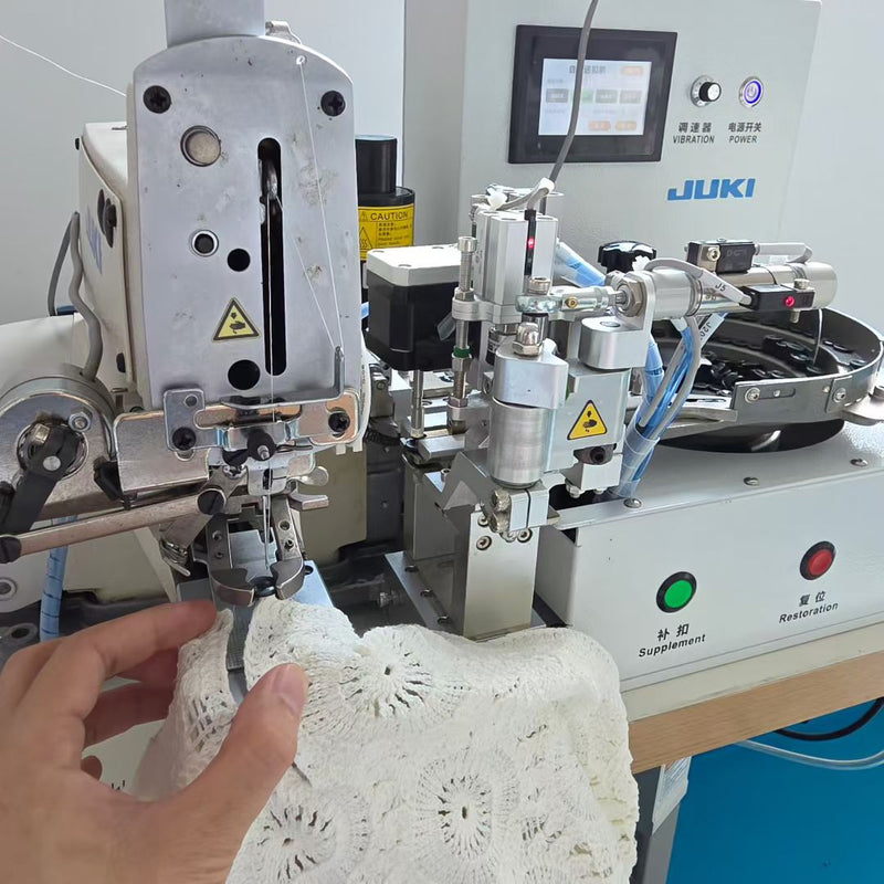 Close-up shot of worker operating JUKI automatic button attaching machine at BENTA factory, processing white crochet lace fabric panels for OEM custom knitwear.