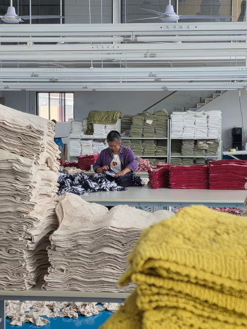 Quality control inspection at BENTA factory, worker checking stacked crochet knitwear fabrics, strict OEM garment quality checking process.